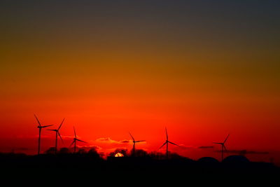 Silhouette of wind turbines on field during sunset