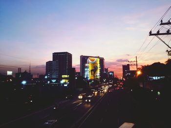 Traffic on road amidst buildings in city against sky during sunset