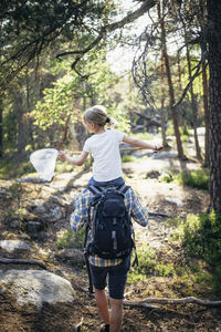 Rear view of father carrying daughter on shoulder in forest