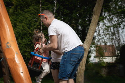 A man pushes a child on a swing in a park on a summer day.