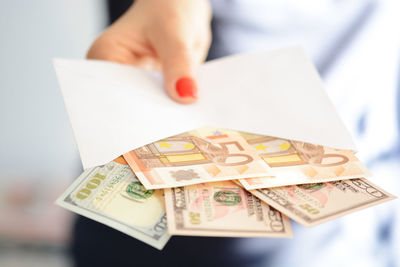 Midsection of woman holding envelope with paper currencies