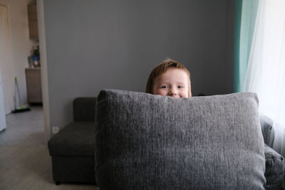 Kid toddler builds house from pillows on sofa in living room, lifestyle and games in real interior