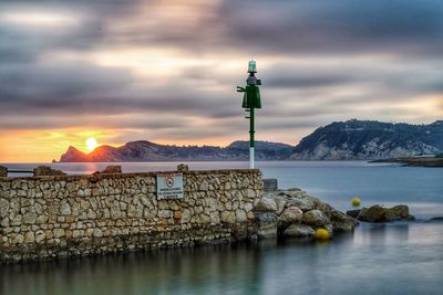 Lighthouse by sea and buildings against sky during sunset