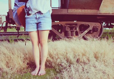 Low section of woman with bag standing by old train on grassy field