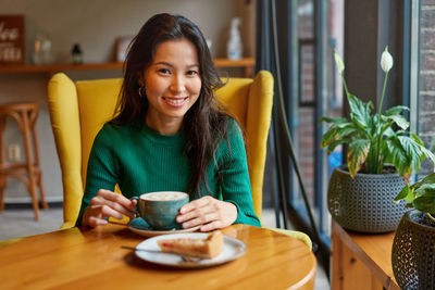 Portrait of young woman using mobile phone while sitting on table