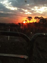 Silhouette trees by road against sky during sunset