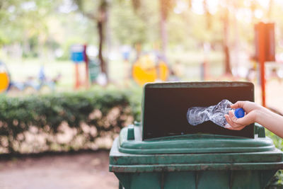 Cropped hand throwing bottle in garbage can