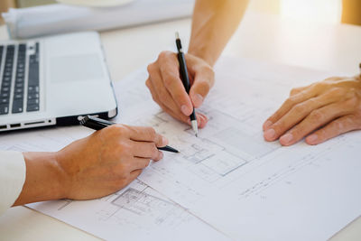 Cropped hands of architects drawing blueprint in office