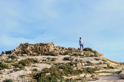 Teenage boy standing on rock formation against sky