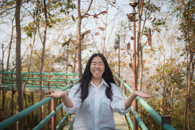 Portrait of smiling young woman standing against trees