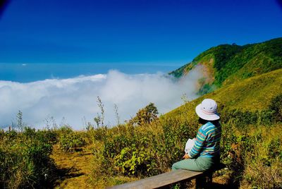 Woman sitting on mountain against sky