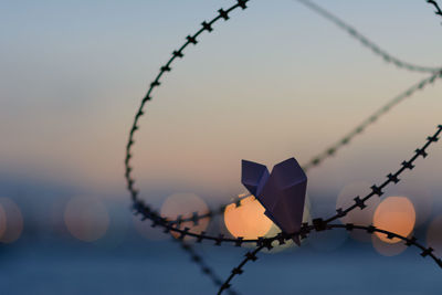 Close-up of barbed wire fence against sky during sunset