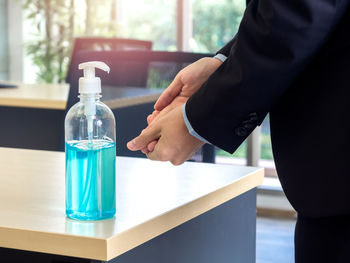 Midsection of woman holding glass bottle on table