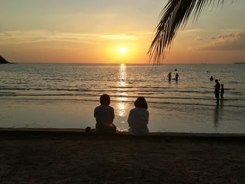 Silhouette people on beach against sky during sunset