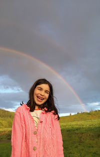 Portrait of smiling woman standing on field against rainbow in sky