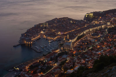 High angle view of illuminated buildings by sea against sky