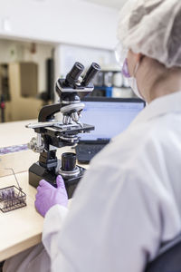 Back view of anonymous woman scientist looking through microscope at laboratory