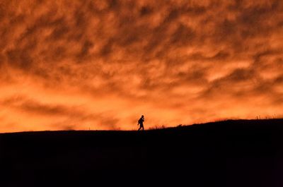 Silhouette man standing on field against sky during sunset