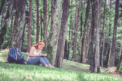 Woman siting on grass and writing in book in forest