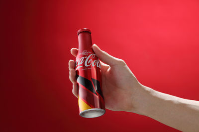 Close-up of hand holding bottle against red background