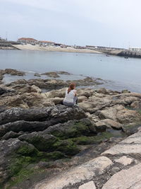 Woman sitting on rock by sea against sky