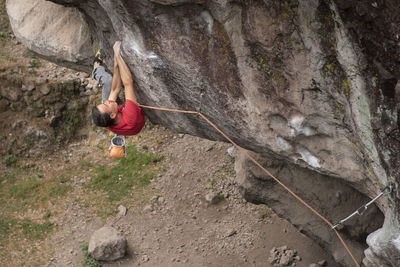 One man wearing red holds with both hands on rock wall while climbing