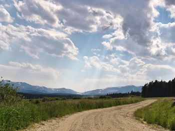 Dirt road amidst field against sky