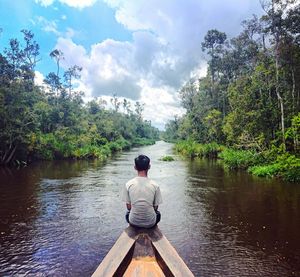 Rear view of man sitting on lake against sky