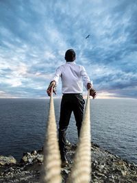 Rear view of man standing in sea against sky
