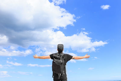 Low angle view of man with arms outstretched standing against sky