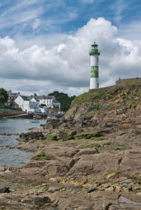 Lighthouse amidst buildings and sea against sky