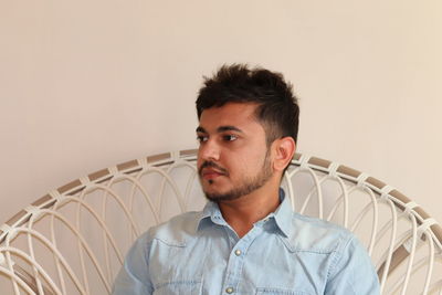 Portrait of young man in denim shirt looking away against wall