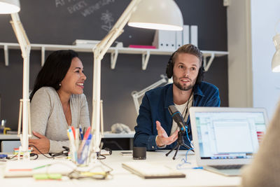 Multi-ethnic business colleagues sitting at desk with laptop and microphone in creative office