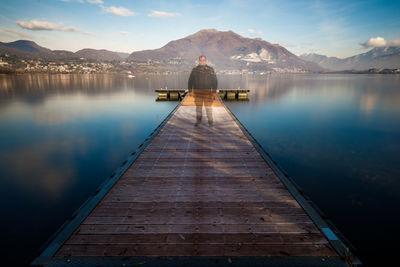 Rear view of man on pier over lake against sky