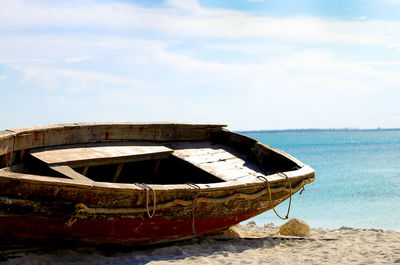 Abandoned boat moored on beach against sky