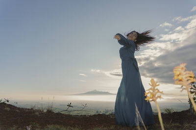 Rear view of woman standing at beach against sky
