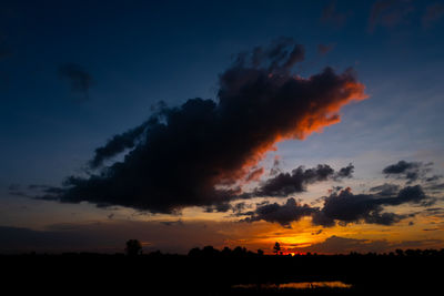 Silhouette trees on field against dramatic sky during sunset