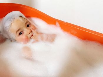 Portrait of smiling baby covered with soap sud in bathtub by wall