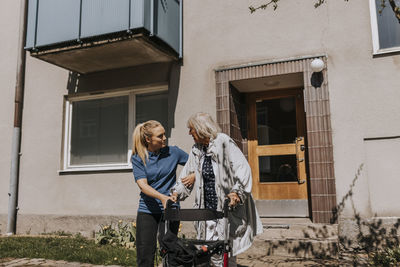 Female caregiver assisting senior woman moving out with walker