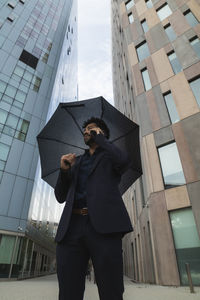 Entrepreneur with umbrella talking on smart phone against building in city