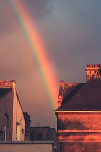 Low angle view of rainbow over houses against sky