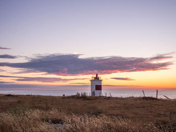 Lighthouse on beach against sky during sunset