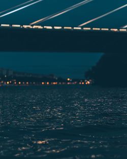 Illuminated bridge over sea against sky at night