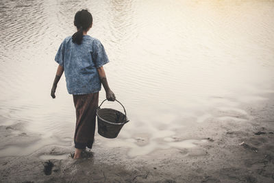 Rear view of girl holding bucket by pond