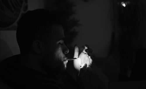Side view of man smoking cigarette at home