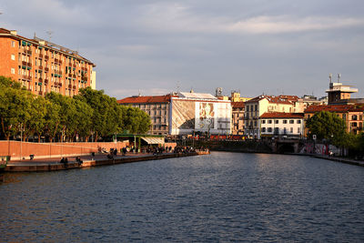 View of buildings by river against cloudy sky