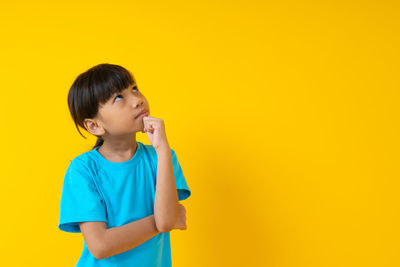 Boy looking away while standing against yellow background