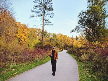 Full length of man standing amidst trees on road during autumn