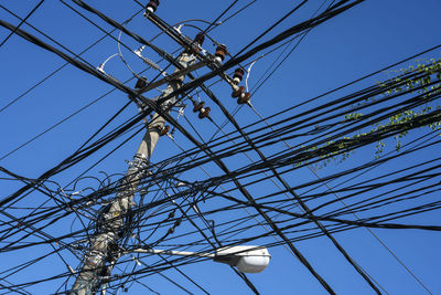 Low angle view of electricity pylon against clear blue sky