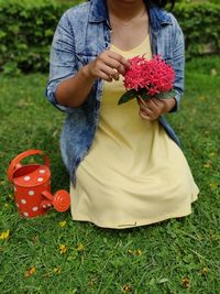 Midsection of woman holding red while standing on field